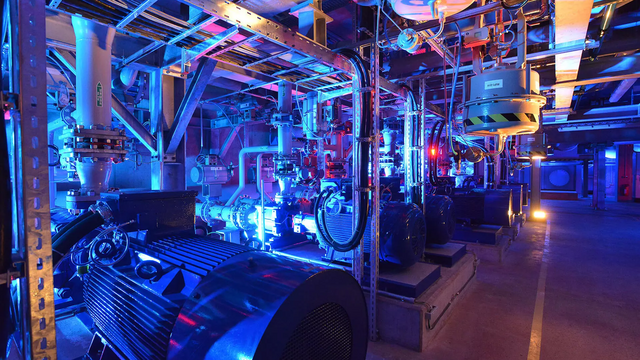 Dunkler Raum mit blauen Lichtern sowie vielen Kabeln und Rohren